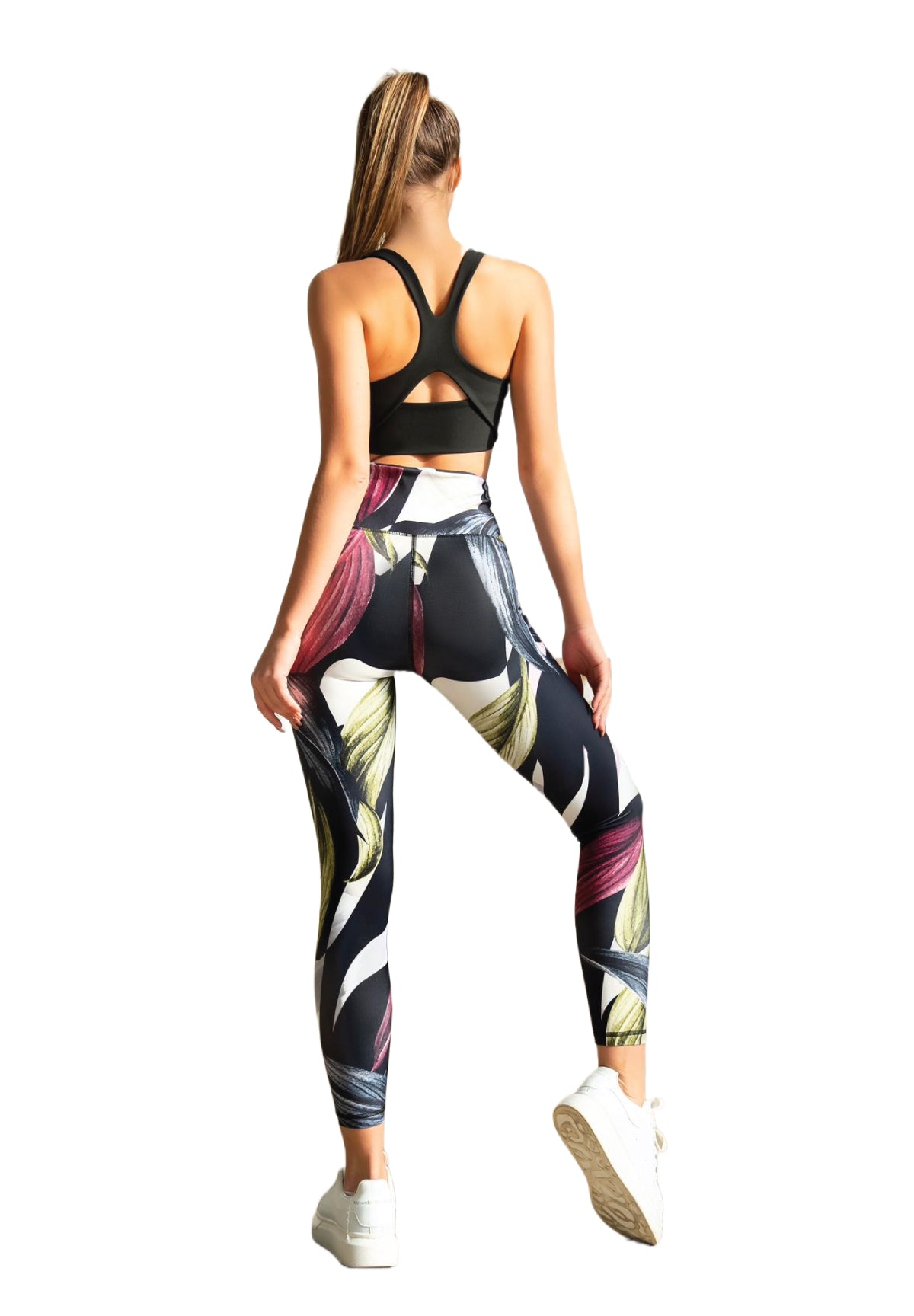 Eine Frau in Lismina 324 Leggings mit extra hoher Taille und Blumenmuster und einem schwarzen Sport-BH steht mit weißen Turnschuhen da.